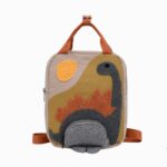 Cartable dinosaure style vintage brodé de forme rectangulaire avec orientation portrait. Un dinosaure vert et orage est brodé sur le devant. Des poignées orange au-dessus. Sur fond gris clair.