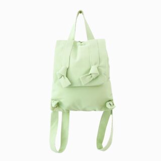 Cartable en coton pour la maternelle de couleur vert anis. Un rabat avec des nœuds comme au bout des bretelles. Sur fond gris clair.