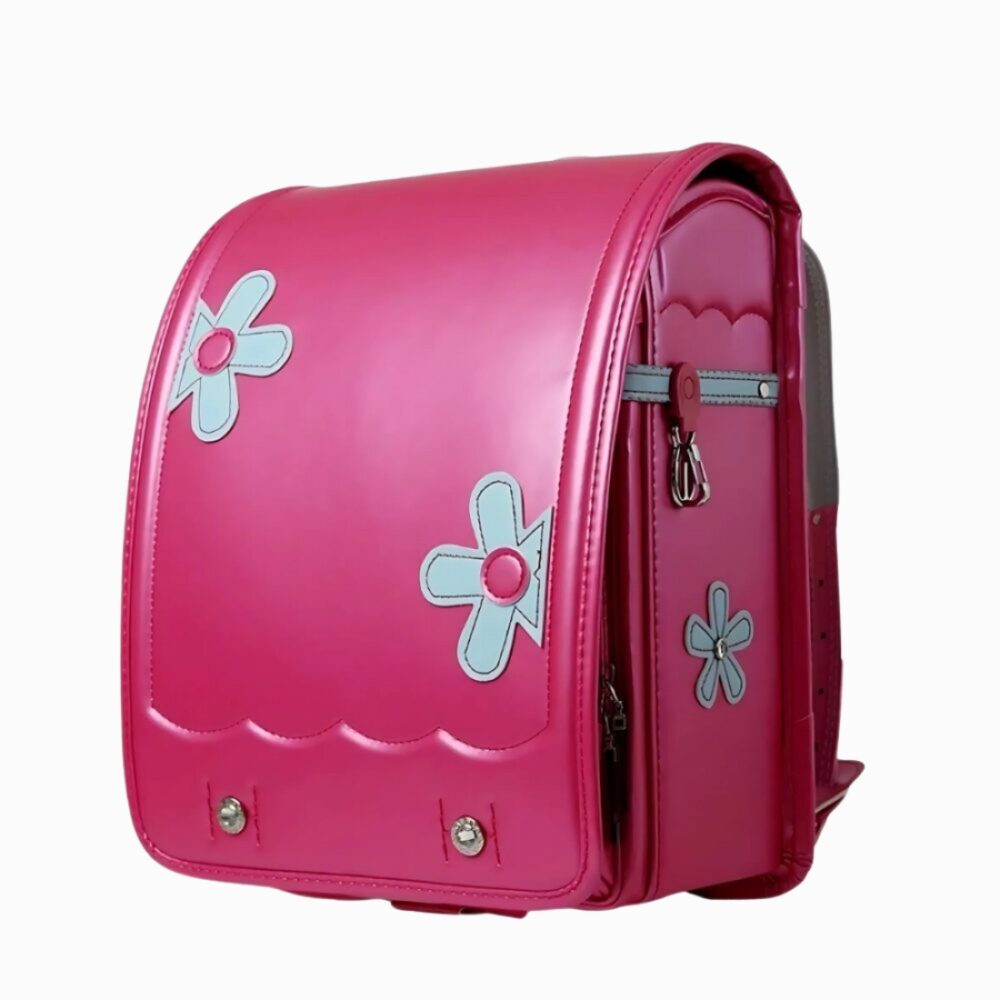 Cartable japonais en cuir synthétique pour fille de couleur rose foncé avec trois fleurs bleu ciel. Sur fond gris clair.