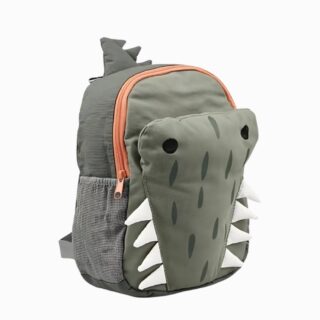 Cartable maternelle en forme de crocodile vert avec les dents blanches en relief. Un compartiment principal et des espaces élastiques sur les côtés. Sur fond gris clair.