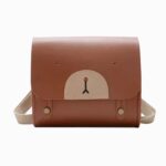 Cartable maternelle en similicuir marron avec un museau d'ourson sur le devant et des bretelles beige. Sur fond gris clair.