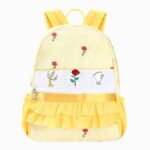 Cartable petite section jaune avec broderie et motif de roses, chandelier et tasse. Sur fond gris clair.