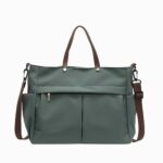 Cartable sac à main en nylon avec bandoulière pour femme de couleur verte avec une bandoulière marron et des anses en cuir synthétique marron. Une poche zippée sur le devant. Sur fond gris clair.