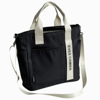 Cartable fourre-tout pour femme avec bandoulière de couleur noire avec la bandoulière, les anses et une bande blanches. Sur fond gris clair.