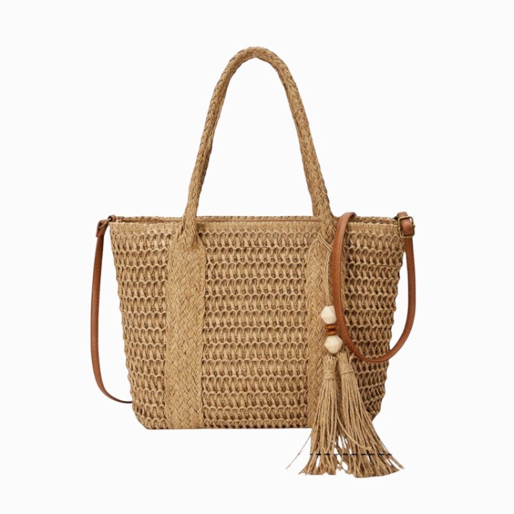 Sac en paille tréssée de forme cabas, avec anse et bandoulière visibles matière effet cuir, avec pampille accorchée sur le devant ; sur fond blanc