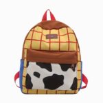 Un cartable Toy Story pour maternelle aux couleurs de Woody, avec un fond jaune à carreaux rouges, une poche blanche et noire façon vache, et des bretelles rouges.
