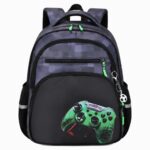 Un cartable CE1 spacieux pour garçon noir et gris, avec plusieurs poches et un dessin de manette de jeu verte, posé sur fond blanc.